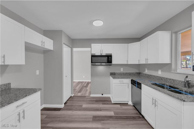 kitchen featuring light stone countertops, light wood-style flooring, a sink, stainless steel appliances, and white cabinetry