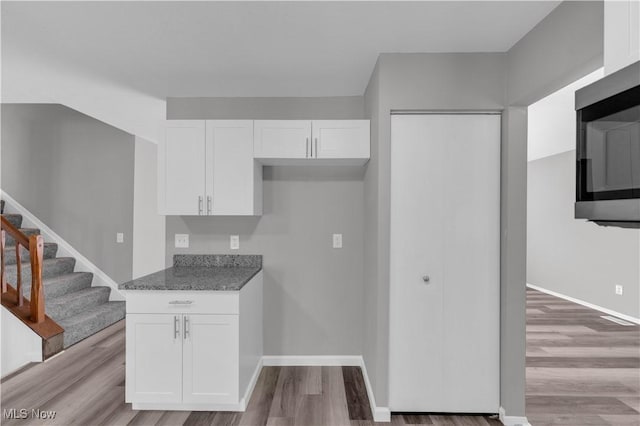 kitchen featuring light wood finished floors, stainless steel microwave, baseboards, dark stone counters, and white cabinets