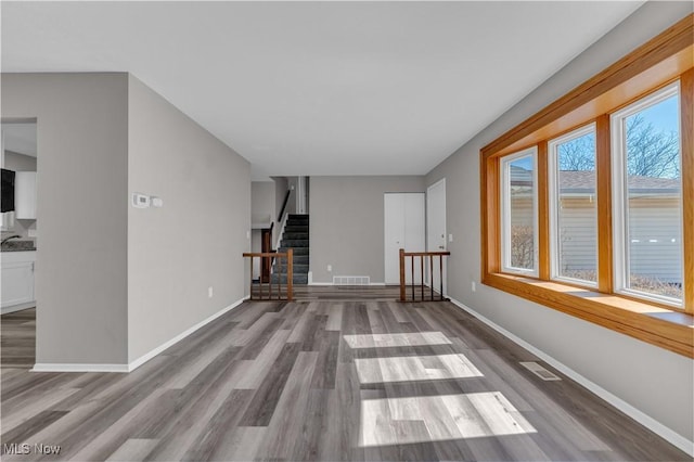 unfurnished living room with visible vents, stairs, baseboards, and wood finished floors