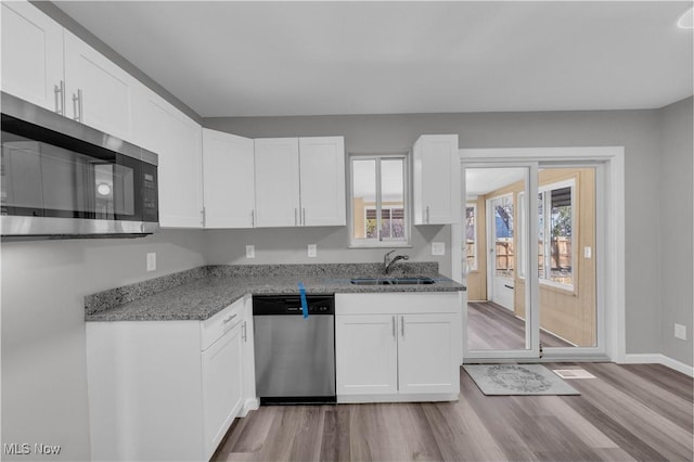 kitchen with light stone counters, appliances with stainless steel finishes, wood finished floors, white cabinetry, and a sink