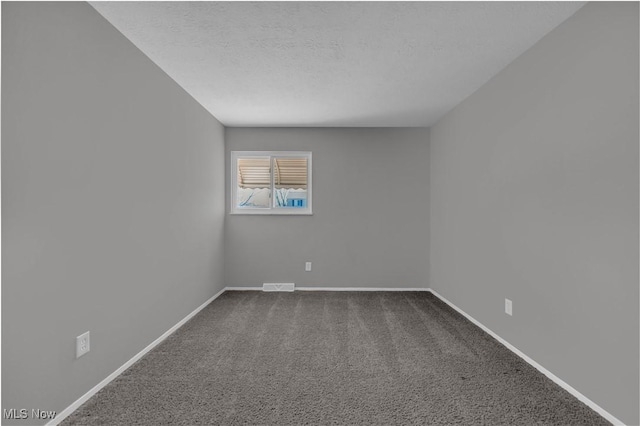 spare room featuring visible vents, baseboards, a textured ceiling, and dark carpet