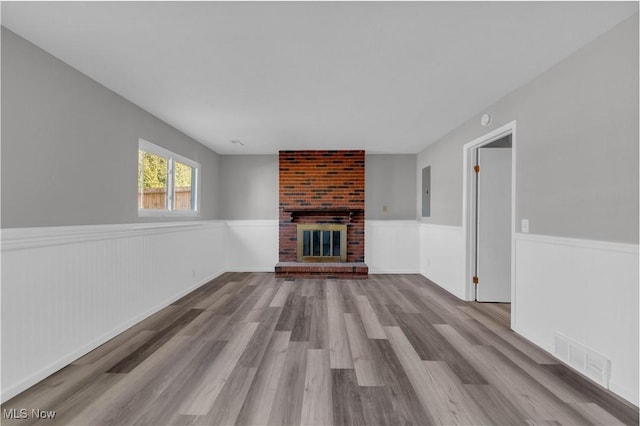 unfurnished living room featuring a wainscoted wall, a fireplace, visible vents, and wood finished floors