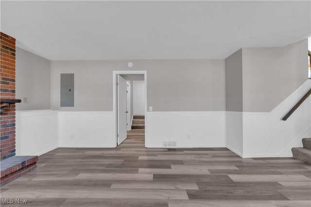 unfurnished living room with stairs, electric panel, a fireplace, and wainscoting