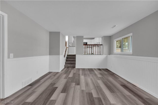 spare room with visible vents, wood finished floors, stairs, and a wainscoted wall