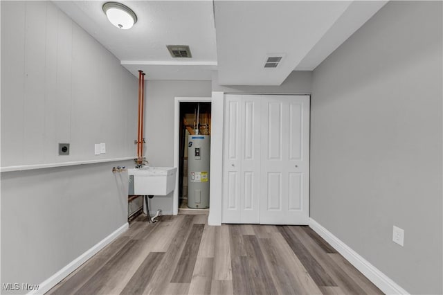 unfurnished bedroom with a closet, visible vents, electric water heater, and wood finished floors