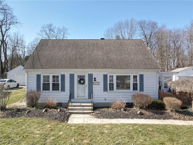 new england style home with a detached garage, roof with shingles, and a front yard