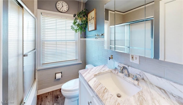 bathroom featuring toilet, vanity, wood finished floors, an enclosed shower, and tile walls