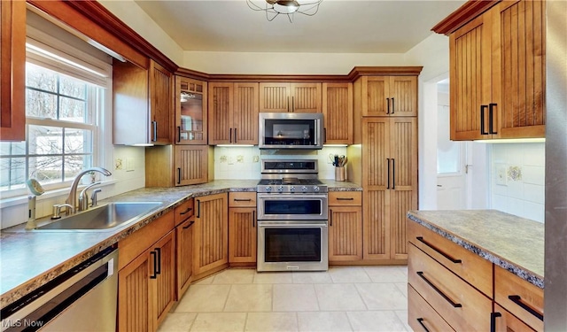 kitchen with tasteful backsplash, glass insert cabinets, light tile patterned floors, appliances with stainless steel finishes, and a sink