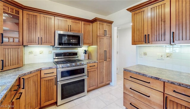 kitchen featuring decorative backsplash, light tile patterned floors, brown cabinetry, and stainless steel appliances