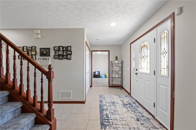 entryway with visible vents, baseboards, stairway, light tile patterned flooring, and a textured ceiling