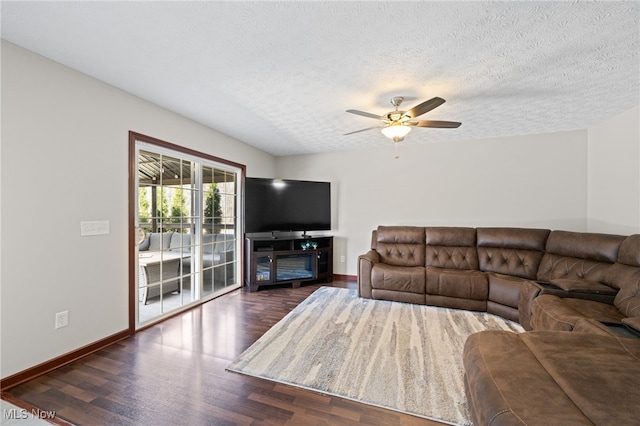 living area featuring dark wood-style floors, a textured ceiling, baseboards, and a ceiling fan