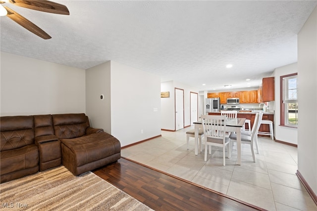 living area with light tile patterned floors, baseboards, a textured ceiling, and a ceiling fan