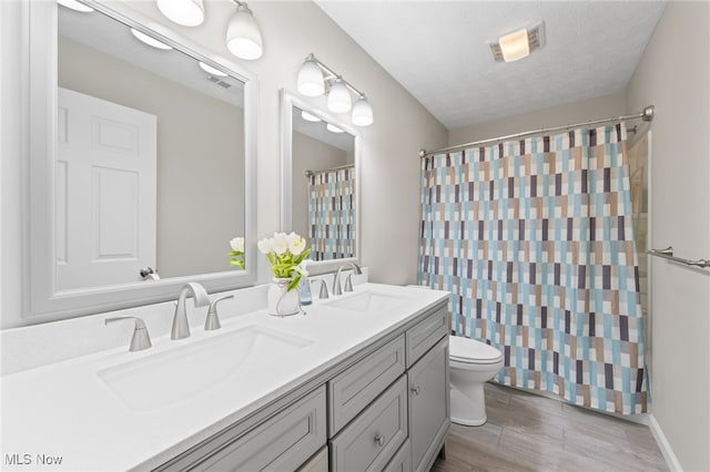 full bathroom with a sink, visible vents, toilet, and double vanity