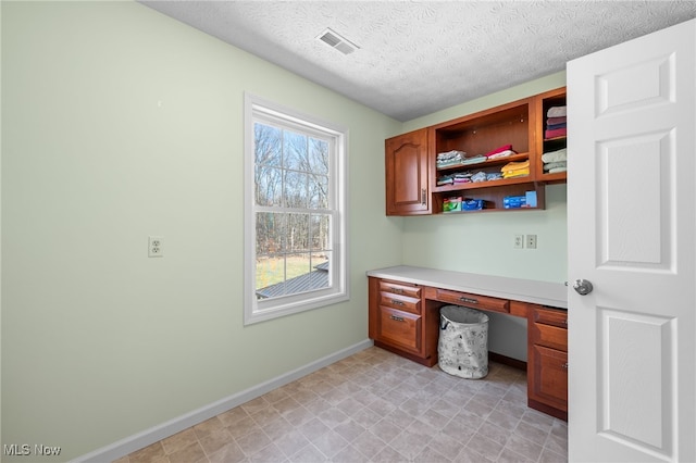 unfurnished office featuring visible vents, a textured ceiling, built in study area, and baseboards