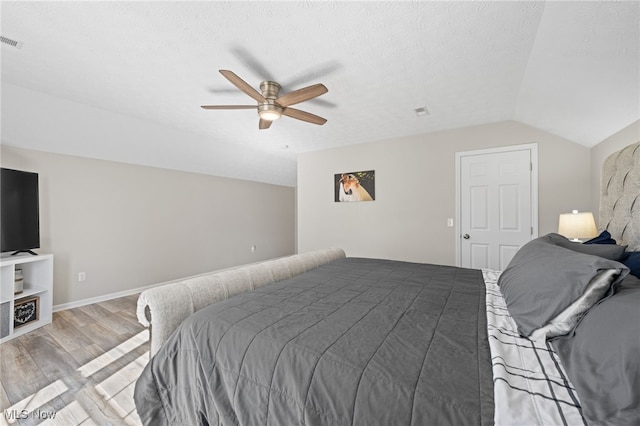 bedroom with visible vents, lofted ceiling, light wood-style floors, a textured ceiling, and a ceiling fan