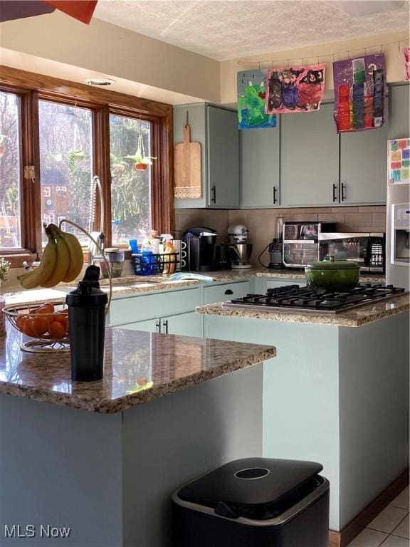 kitchen with light tile patterned floors, stone counters, a peninsula, a textured ceiling, and backsplash