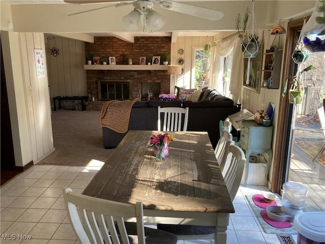 dining space featuring wooden walls, light colored carpet, a fireplace, light tile patterned flooring, and a ceiling fan