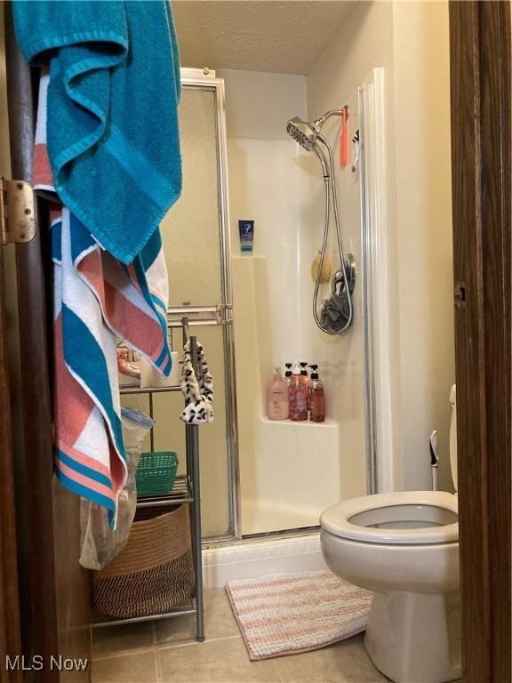 bathroom featuring tile patterned flooring, toilet, a stall shower, and a textured ceiling