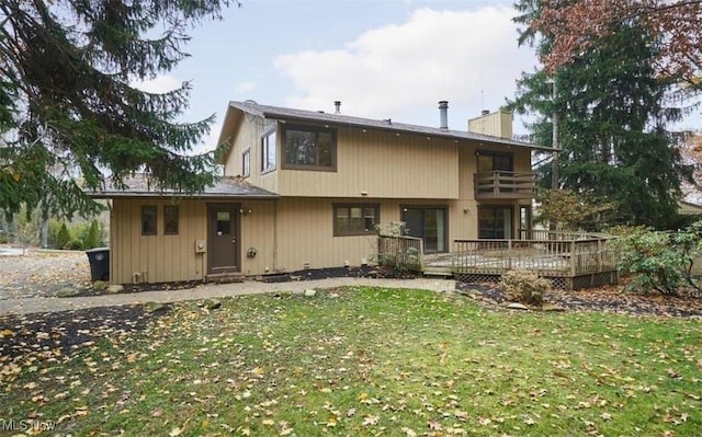 back of house featuring a deck, a balcony, a yard, and a chimney