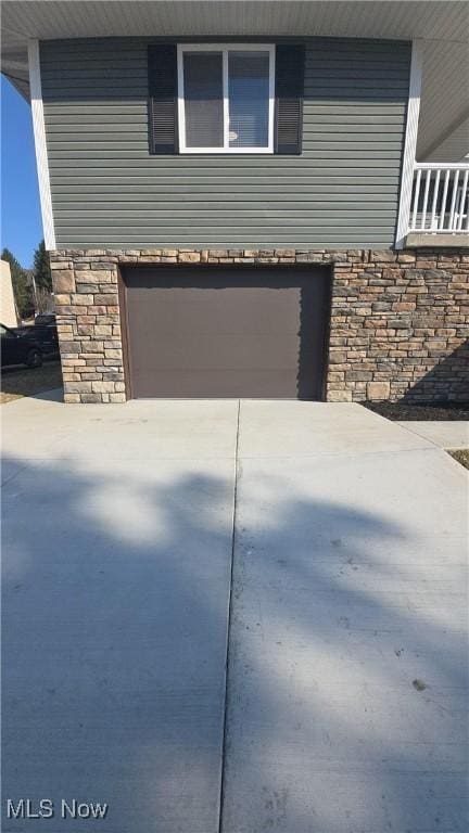 view of property exterior featuring stone siding, driveway, and an attached garage