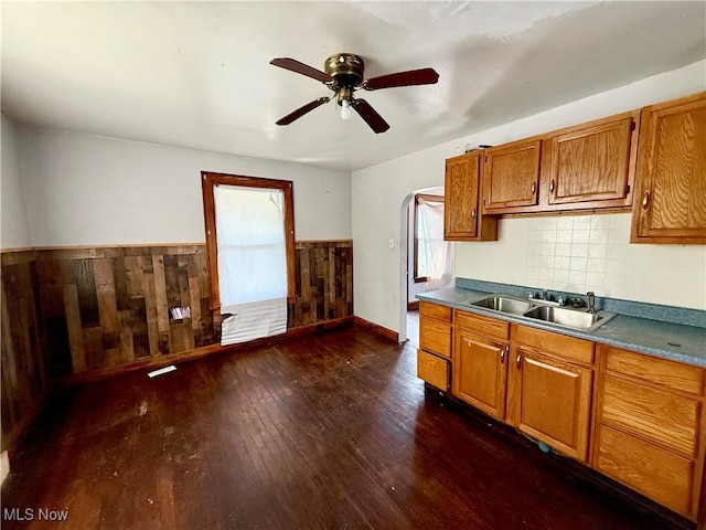 kitchen with brown cabinets, dark wood-type flooring, a sink, arched walkways, and wainscoting