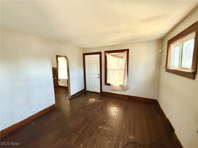 spare room featuring baseboards, arched walkways, and hardwood / wood-style floors