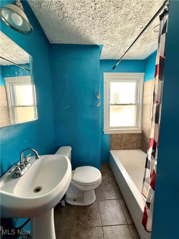 bathroom featuring a sink, toilet, a textured ceiling, and tile patterned flooring