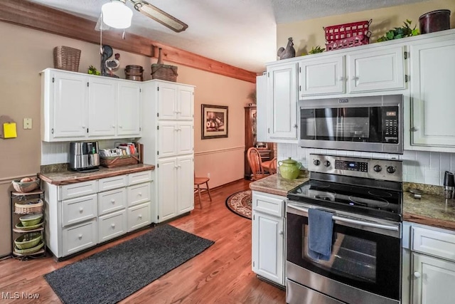 kitchen with light wood-style flooring, ceiling fan, decorative backsplash, appliances with stainless steel finishes, and white cabinetry