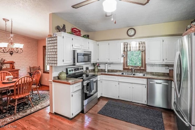 kitchen with wood finished floors, a sink, stainless steel appliances, white cabinetry, and ceiling fan with notable chandelier