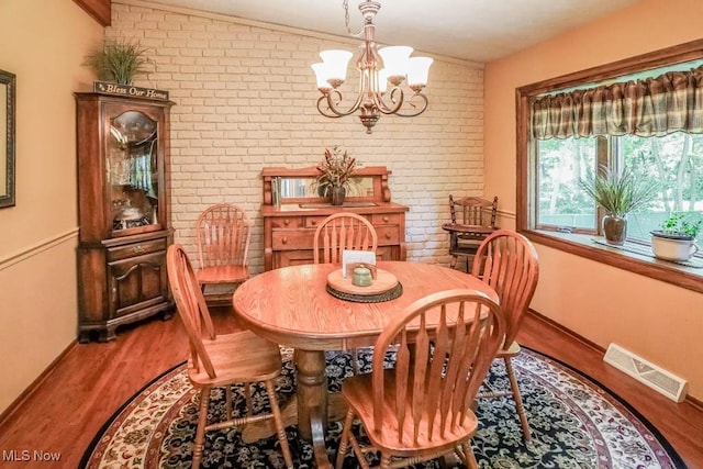 dining room featuring wood finished floors, visible vents, brick wall, and a chandelier