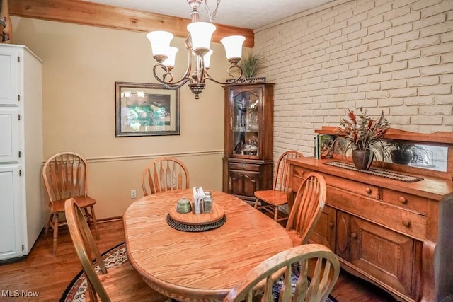 dining room featuring an inviting chandelier, wood finished floors, and brick wall