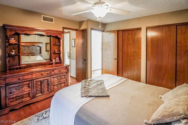 bedroom with a ceiling fan, wood finished floors, visible vents, multiple closets, and a textured ceiling