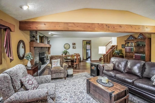 living room with stairs, lofted ceiling with beams, a stone fireplace, and wood finished floors