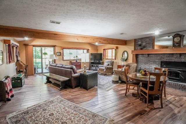 living area featuring hardwood / wood-style floors, visible vents, a wood stove, a textured ceiling, and beamed ceiling