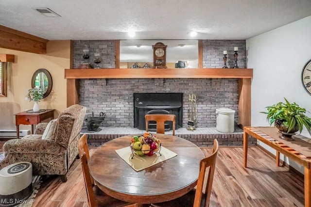 interior space featuring a baseboard heating unit, light wood-style floors, visible vents, and a textured ceiling