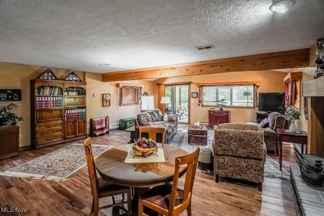 dining area featuring visible vents, beam ceiling, light wood-style flooring, a textured ceiling, and a baseboard radiator