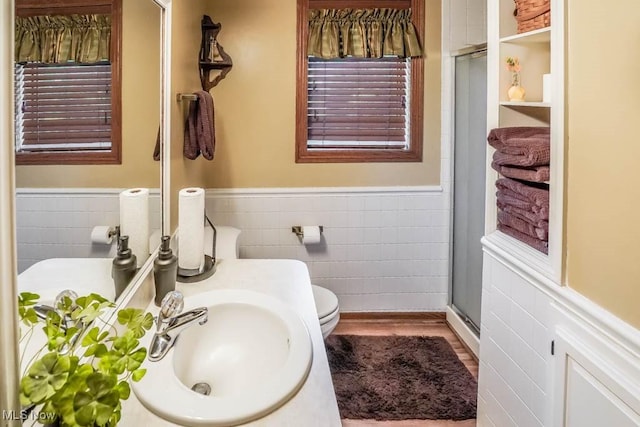 bathroom featuring a shower stall, wood finished floors, tile walls, and a wainscoted wall