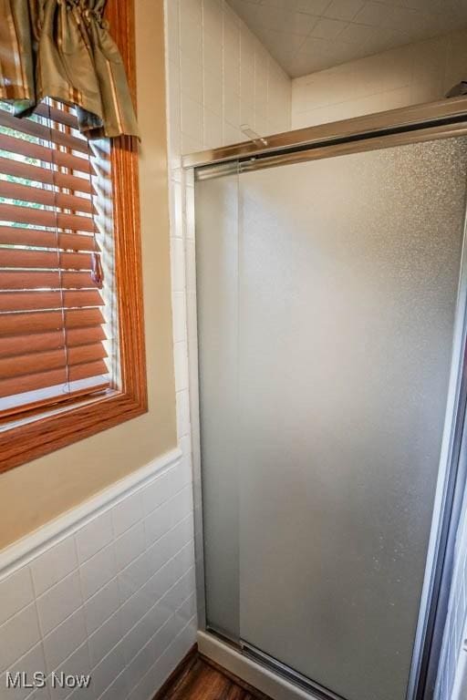 bathroom with a wainscoted wall, tile walls, and a shower stall