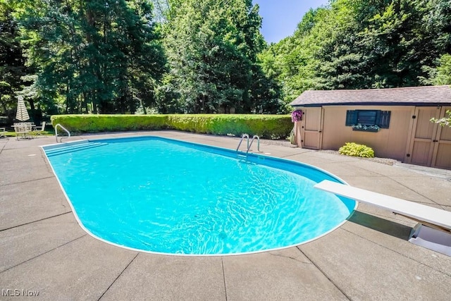 pool with a patio, an outbuilding, and a diving board