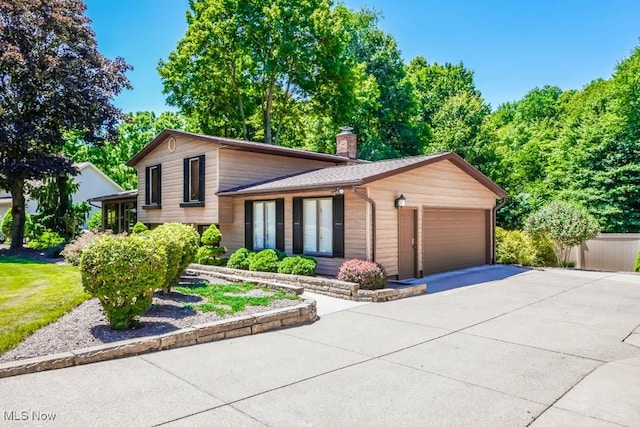 split level home featuring an attached garage, a chimney, and concrete driveway