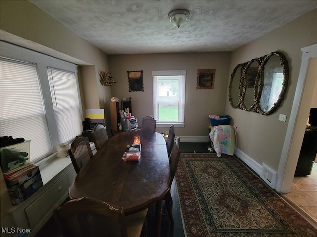 dining space with tile patterned floors, visible vents, a textured ceiling, and baseboards