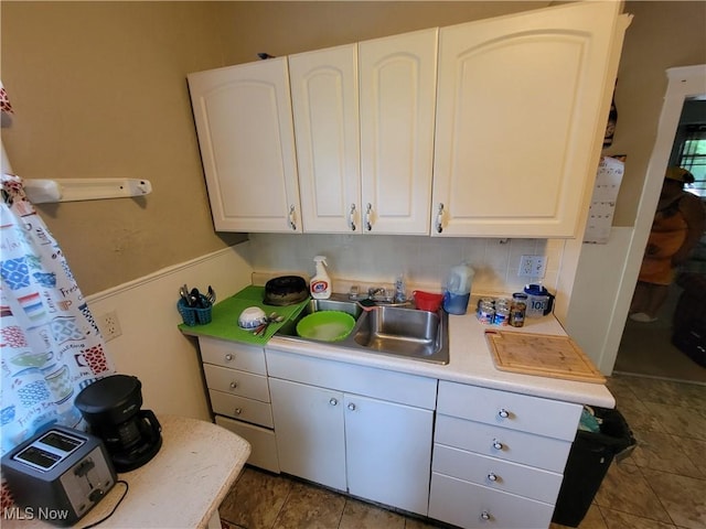 kitchen with tasteful backsplash, white cabinets, light countertops, and a sink