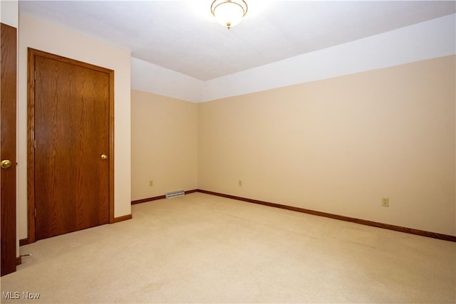 spare room featuring visible vents, light carpet, lofted ceiling, and baseboards