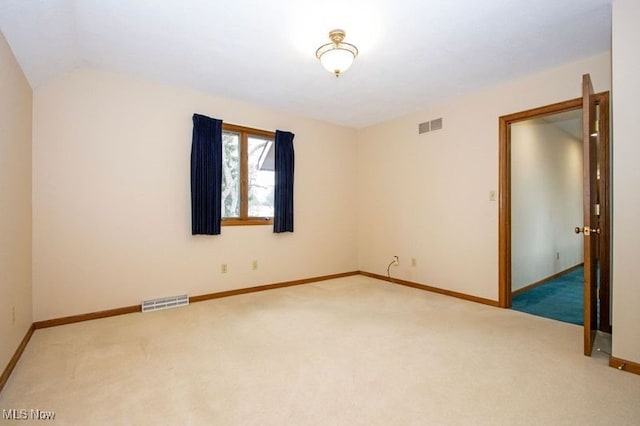 carpeted empty room featuring visible vents, baseboards, and lofted ceiling