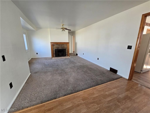 unfurnished living room featuring wood finished floors, a ceiling fan, baseboards, carpet floors, and a fireplace