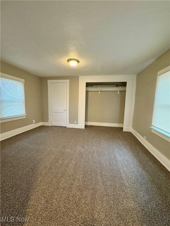 unfurnished bedroom with dark colored carpet, a closet, baseboards, and a textured ceiling