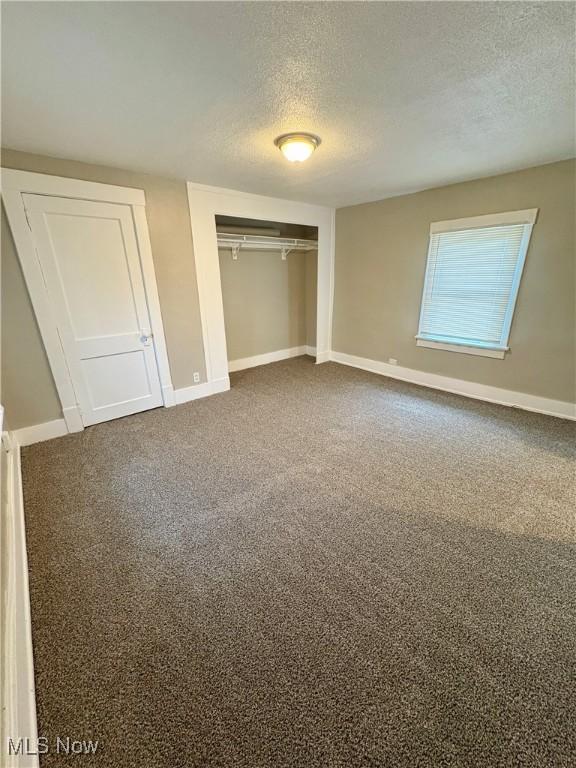 unfurnished bedroom with dark carpet, a textured ceiling, and baseboards