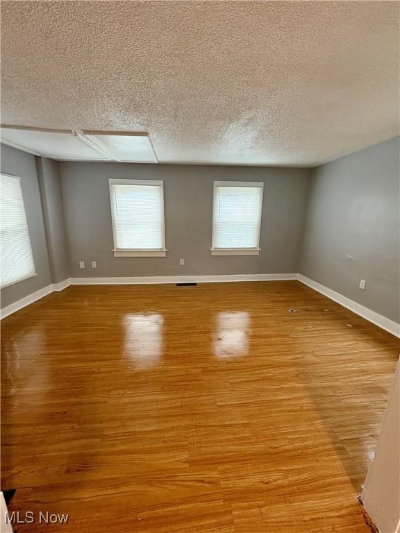 spare room featuring a wealth of natural light, light wood finished floors, a textured ceiling, and baseboards