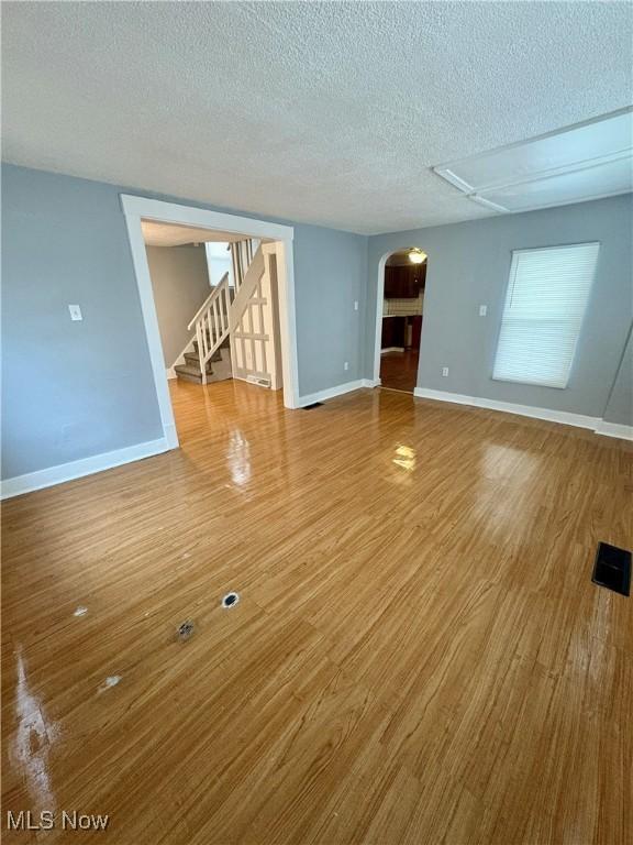 unfurnished living room with stairway, arched walkways, a textured ceiling, and wood finished floors