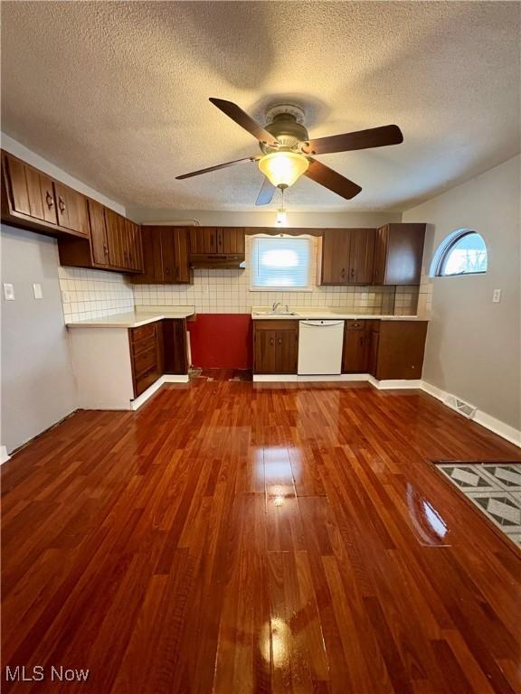 kitchen featuring tasteful backsplash, dark wood-type flooring, light countertops, white dishwasher, and a ceiling fan